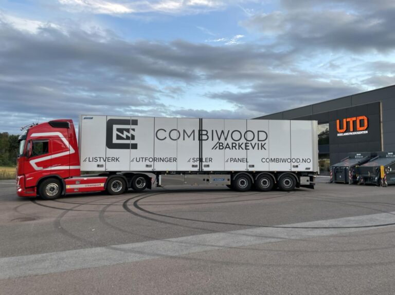 Rød og hvit lastebil med tilhenger merket Combiwood Barkevik, parkert foran bygning med UTD-logo