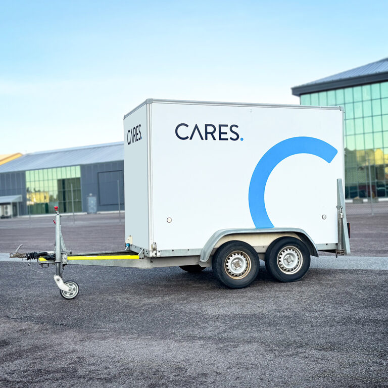 Hvit kassehenger med utskåret foliedekor. Blå halvsirkel og Cares logo