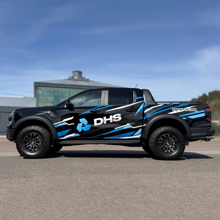 Sort Ford Ranger Raptor sett fra siden med bilreklame og dekor for DHS. Blå og hvite stripete detaljer.