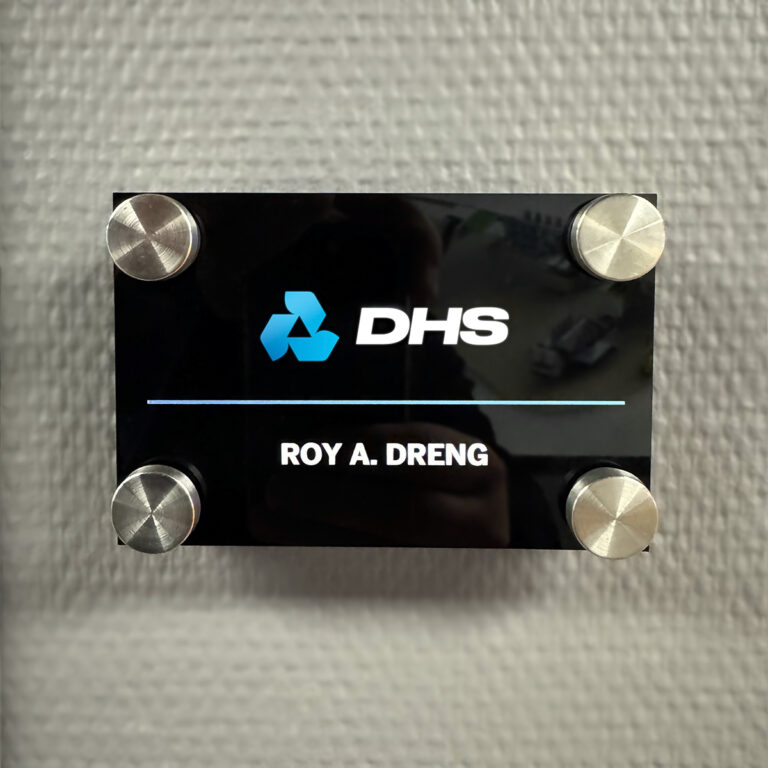 Nærbilde av innvendig akrylskilt. Sort skilt med DHS logo og 4 avstandsstykker