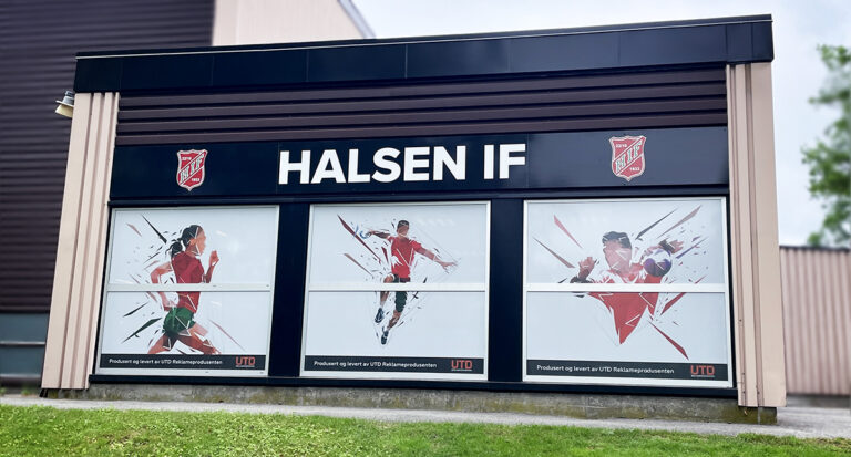 Fasadebilde av Bergslihallen med sorte plateskilt for Halsen IF og Oneway Vision printet folie på vinduer for utsyn uten innsyn.