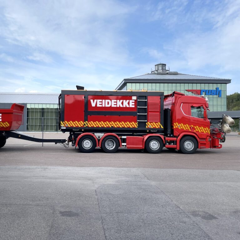 Stor, rød lastebil med henger foliert for Veidekke - lastebildekor sett fra siden