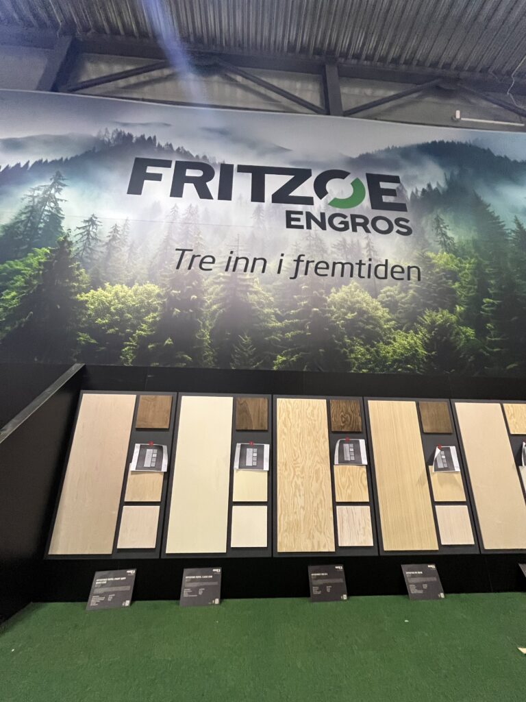 Fritzøe Engros utstilling med skogslandskap bakgrunn og teksten "Tre inn i fremtiden", samt utstillingsvegg med treprodukter og prøver
