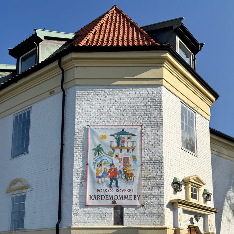 Stort banner for Folk og Røvere i Kardemomme By som henger på fasaden til Teaterhuset Munken i Larvik