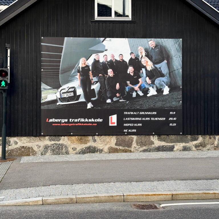Stort printet PVC-banner hengende på en mørk husvegg for Løbergs Trafikkskole