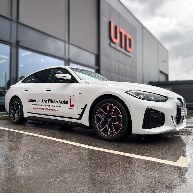 Hvit BMW med utskåret bilreklame på siden for Løbergs Trafikkskole stående utenfor UTD Reklameprodusenten