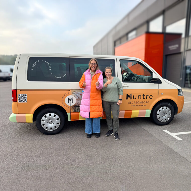 To smilende kvinner foran en helfoliert ID Buzz for Muntre Eldreomsorg.