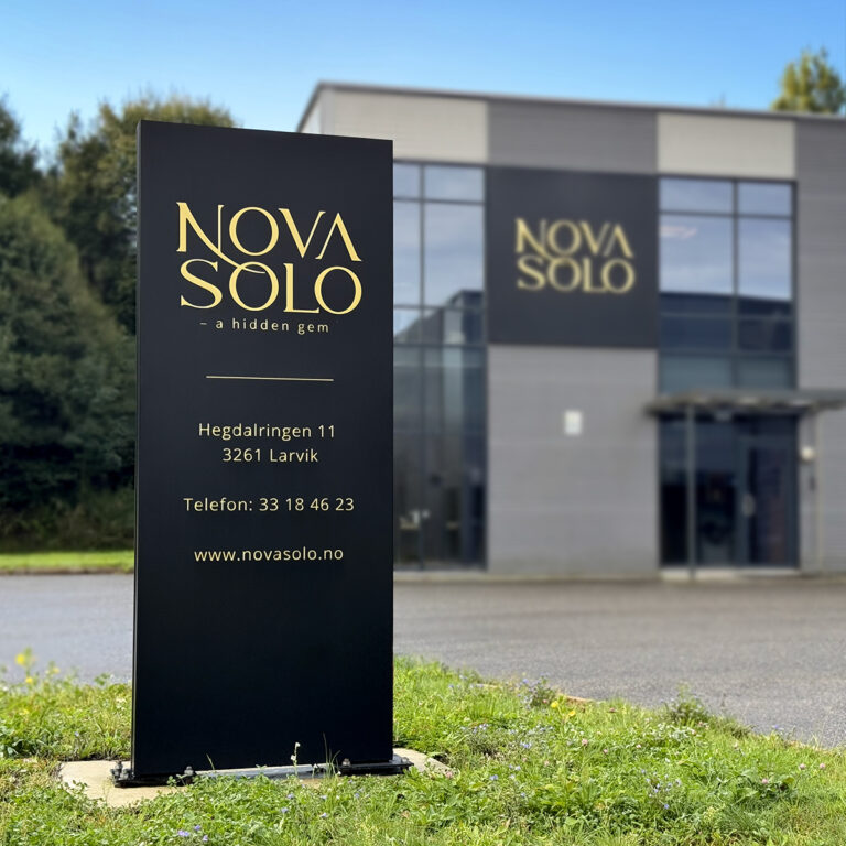 Sort LED-skilt pylon ved innkjøring til Novasolo. Lysskilt på fasaden i bakgrunnen
