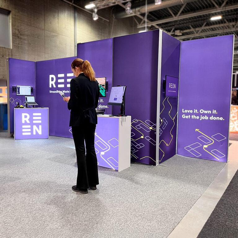 Kvinne stående foran messestand for Reen. Messevegger med lyskasser i aluminium og tekstilduker med trykk.