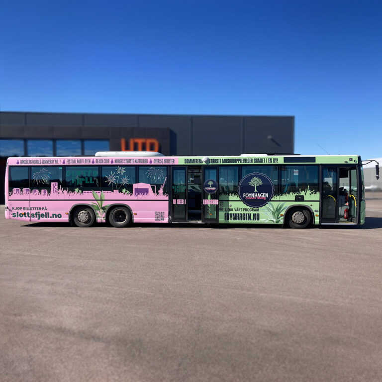 Helfoliert buss sett fra siden foran næringslokalene til UTD Reklameprodusenten. Bussreklamen er for Foynhagen og Slottsfjell Festivalen