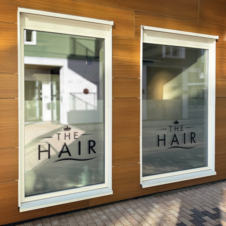 To vinduer med frostet folie innvendig og utskåret sort logo utvendig for The Hair i Larvik