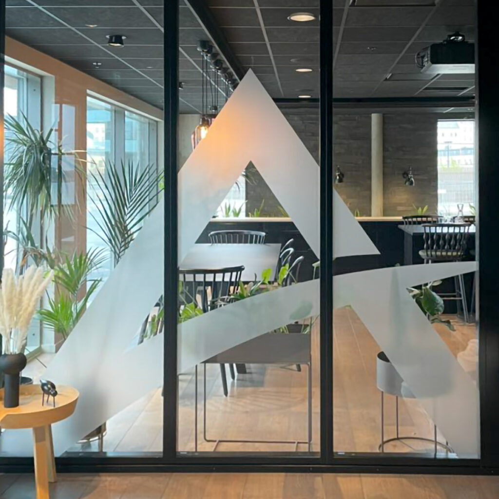 Stort glassfelt med utskåret logosymbol i frostet folie for Atenti