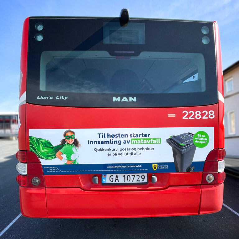 Buss sett bakfra i trafikken med et lite liggende reklamefelt med budskap fra Saprsborg Kommune om innsamling av matavfall