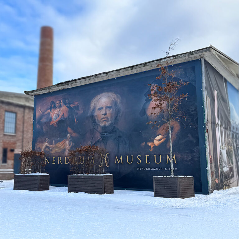 Stort mørkt banner for Nerdrum Musem som henger på hele fasaden av et hus.