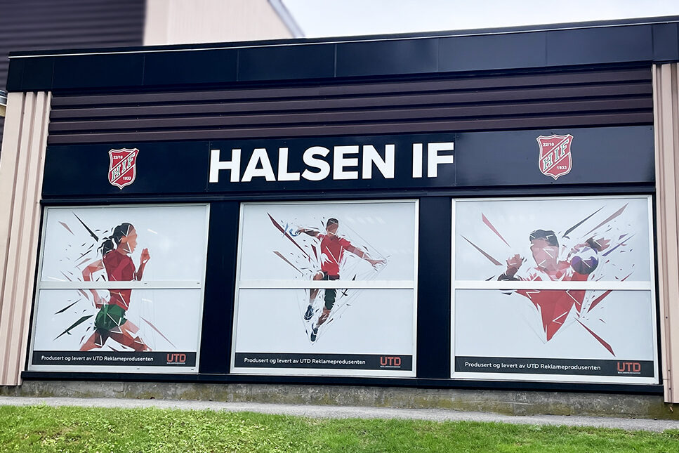 Fasadebilde av Bergslihallen med sorte plateskilt for Halsen IF og Oneway Vision printet folie på vinduer for utsyn uten innsyn.