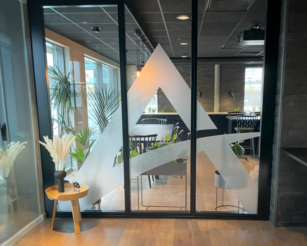 Stort glassfelt med utskåret logosymbol i frostet folie for Atenti