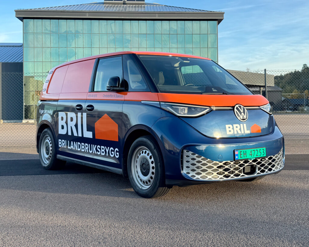Helfoliert ID Buzz sett skrått forfra. To-farget med blått nederst og oransje øverst og stor BRI Landbuksbygg logo
