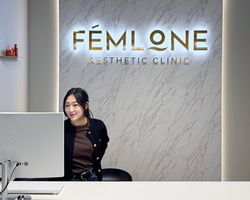 Kvinne i resepsjon foran stort innvendig skilt i marmormønster med bakbelyst logo, LED-skilt, Femlone Aesthetic Clinic
