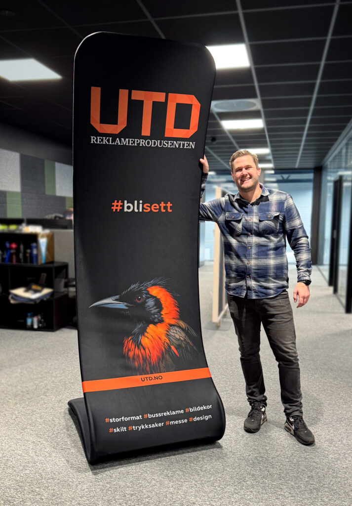 S-formet display med logo UTD Reklameprodusenten og visuelle elementer med en mann stående ved siden av