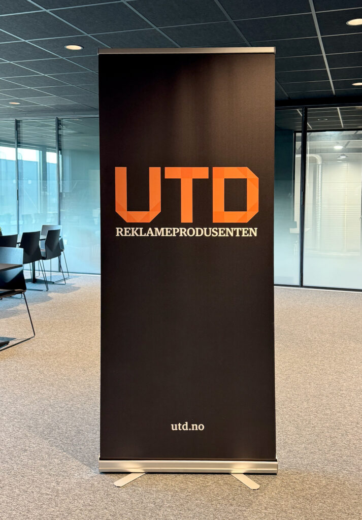 rollup med sort bakgrunn og UTD Reklameprodusenten logo i oransje inne i kontorområde
