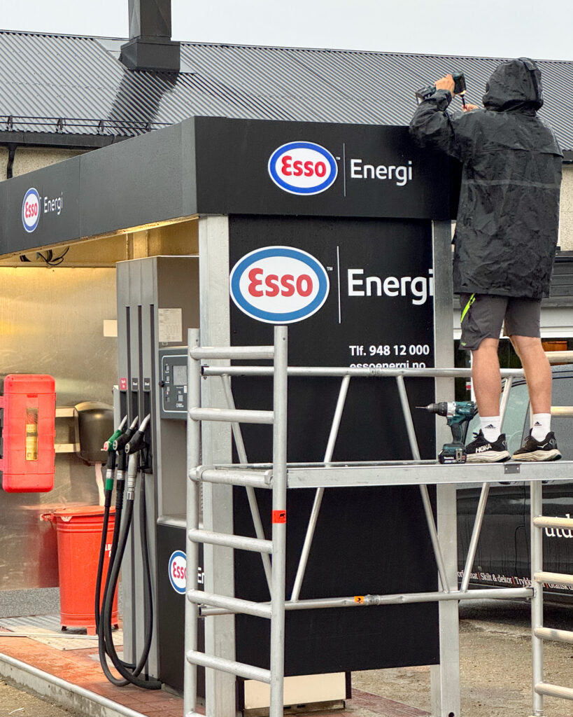 UTD-montør monterer Esso Energi LED-skilt på baldakin i regnvær – feltmontering pumpestasjon Midt-Norge