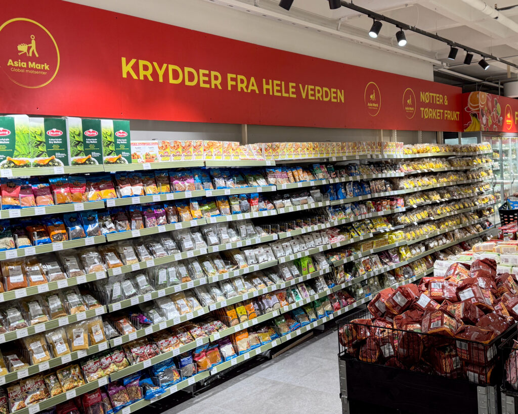Innvendig kategorisskilt med teksten «Krydder fra hele verden» over fylte hyllerader — innvendig butikkprofilering Asia Mark