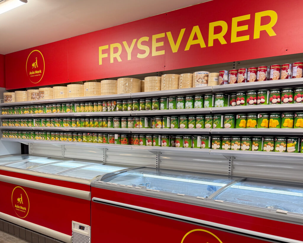Asia Mark «Frysevarer»-skilt i rød bakgrunn med gul tekst og logo over frysedisker — innvendig butikkskilting